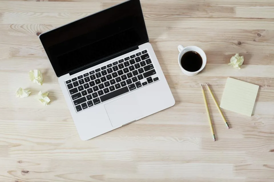 Un ordinateur portable, un carnet et un café posés sur un bureau clair : six façons de se faire accompagner